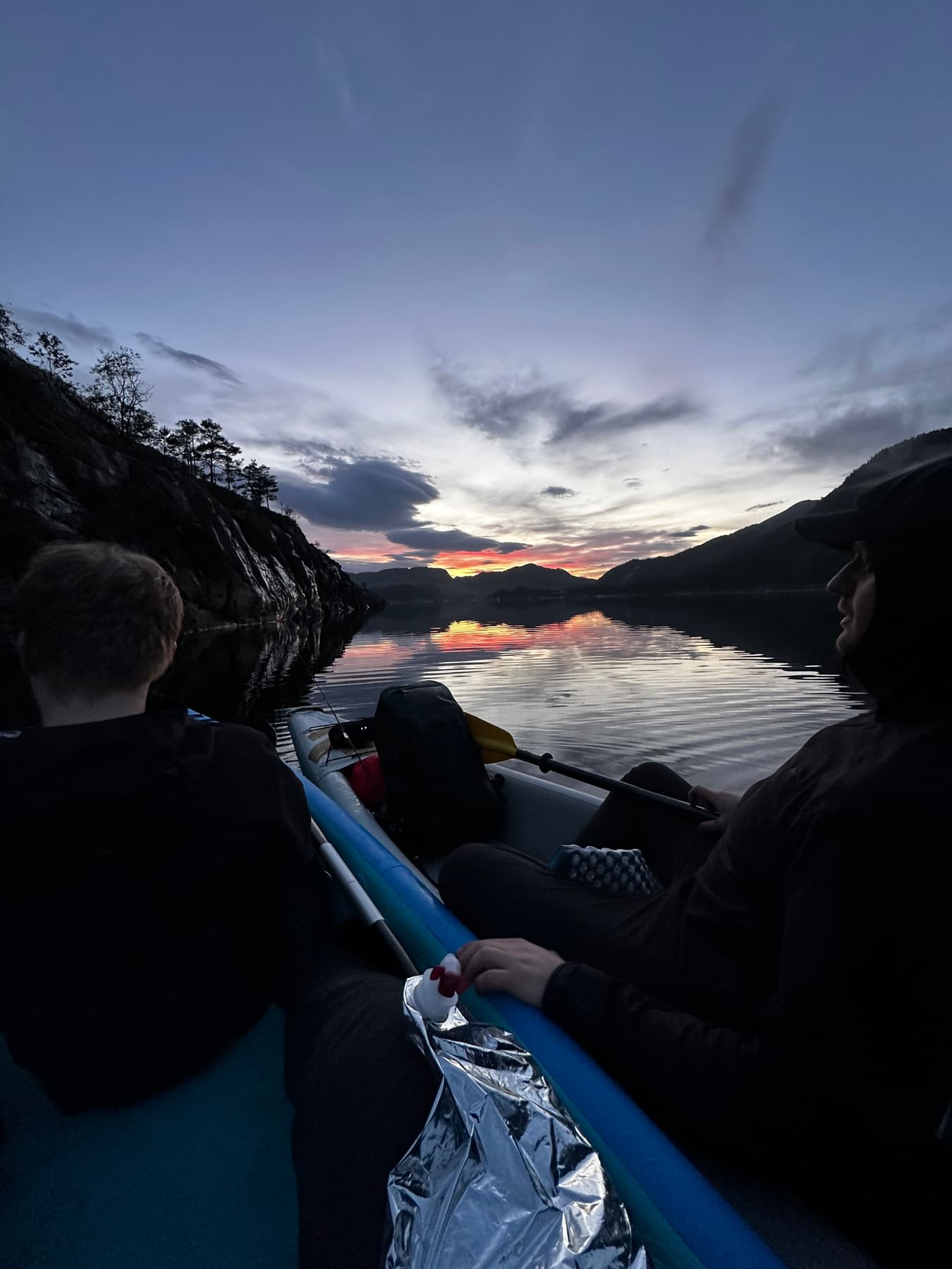 Two people kayaking on a fjord at sunset