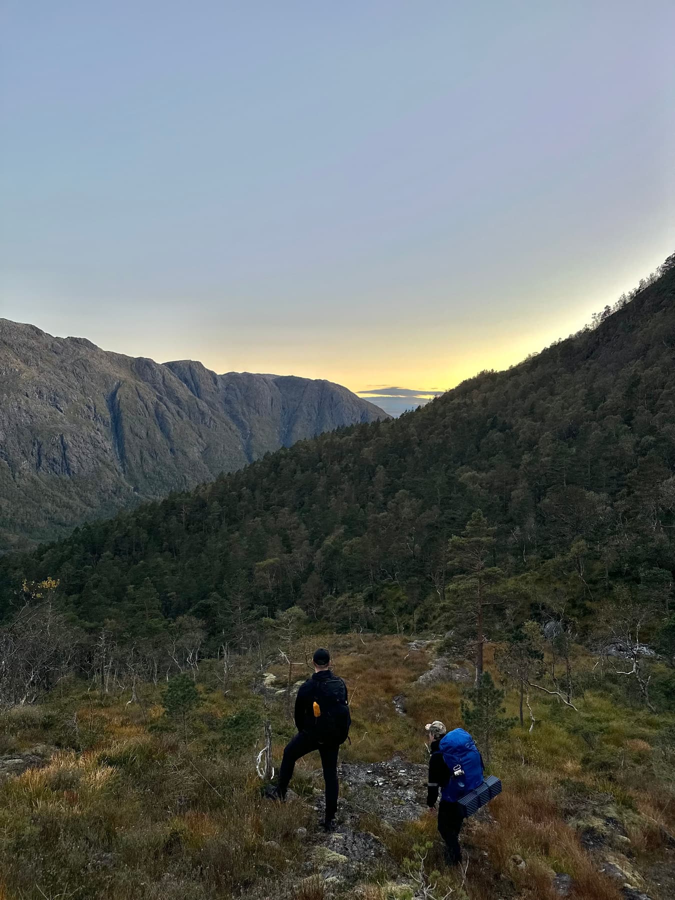 Two hikers heading toward a valley at dusk